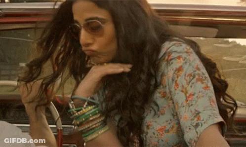 A Woman With Long Hair And Sunglasses Is Sitting In A Car . GIF