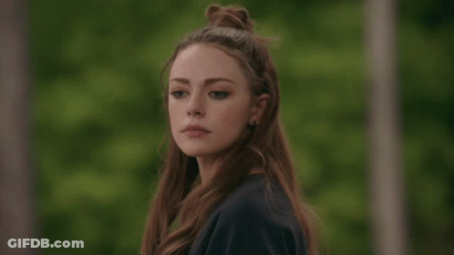 A Woman With Long Hair In A Bun Looks At The Camera GIF