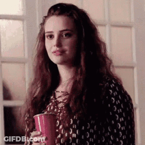 A Woman With Long Hair Is Holding A Red Cup In Her Hand And Looking At The Camera . GIF