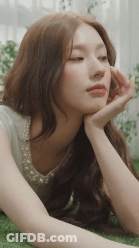 A Woman With Long Hair Is Laying On The Grass With Her Hand On Her Face GIF