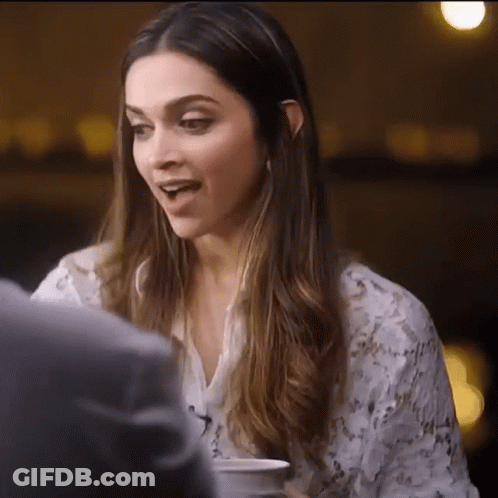 A Woman With Long Hair Is Sitting At A Table With A Cup Of Coffee In Her Hand . GIF