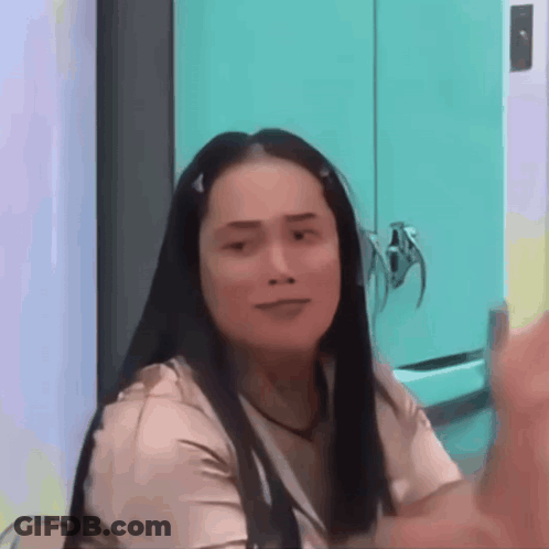 A Woman With Long Hair Is Sitting In Front Of A Blue Cabinet And Making A Funny Face . GIF