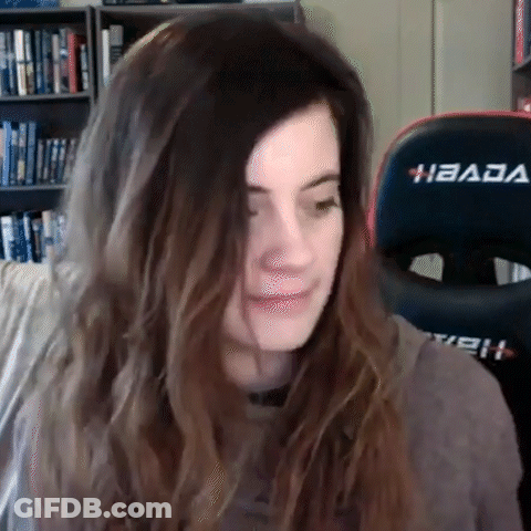 A Woman With Long Hair Is Sitting In Front Of A Gaming Chair And Making A Funny Face . GIF