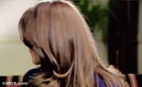 A Woman With Long Hair Is Sitting On A Couch Looking Over Her Shoulder GIF