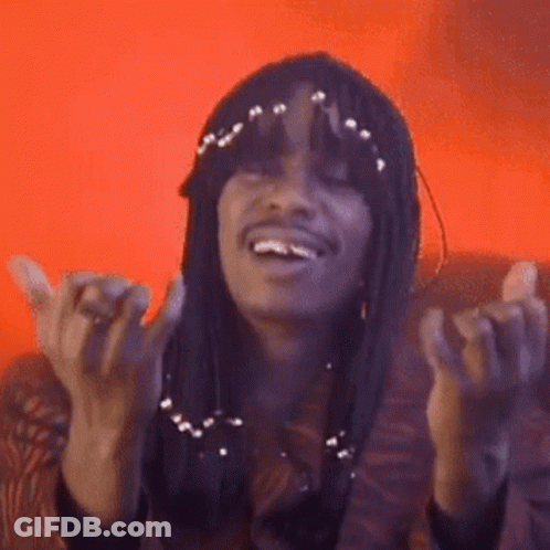 A Woman With Long Hair Is Sitting On A Couch With Her Hands In The Air And Smiling . GIF