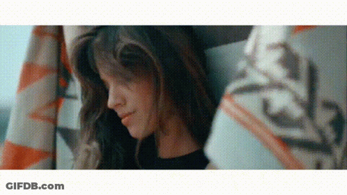 A Woman With Long Hair Is Sitting Under A Blanket And Smiling . GIF