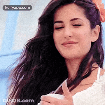 A Woman With Long Hair Is Smiling And Holding A Cup Of Coffee . GIF