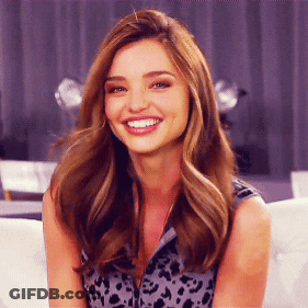 A Woman With Long Hair Is Smiling And Wearing A Leopard Print Top GIF