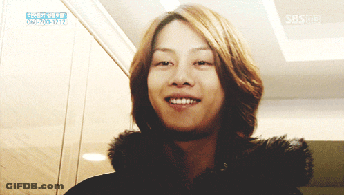 A Woman With Long Hair Is Smiling In Front Of A Sign That Says Sbs On It GIF