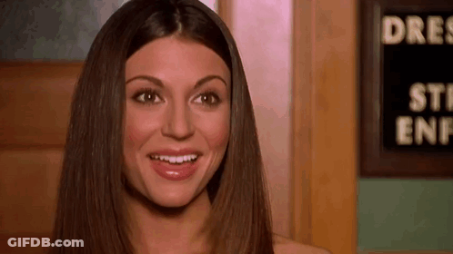 A Woman With Long Hair Is Smiling In Front Of A Sign That Says `` Steak Enf '' . GIF