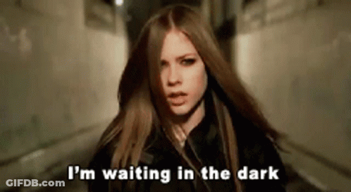 A Woman With Long Hair Is Standing In A Dark Alleyway And Saying I 'M Waiting In The Dark . GIF