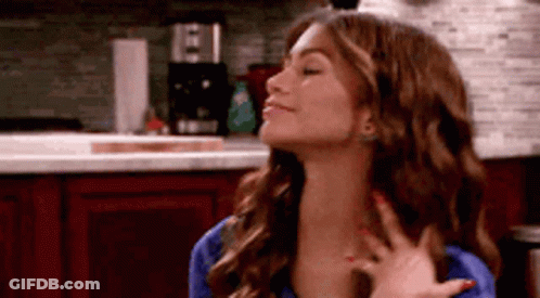 A Woman With Long Hair Is Standing In A Kitchen With Her Eyes Closed And Her Hand On Her Neck . GIF