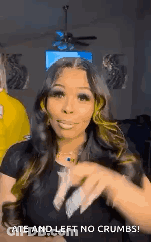 A Woman With Long Hair Is Standing In A Living Room With A Ceiling Fan In The Background . GIF