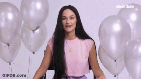 A Woman With Long Hair Is Standing In Front Of A Bunch Of Balloons . GIF