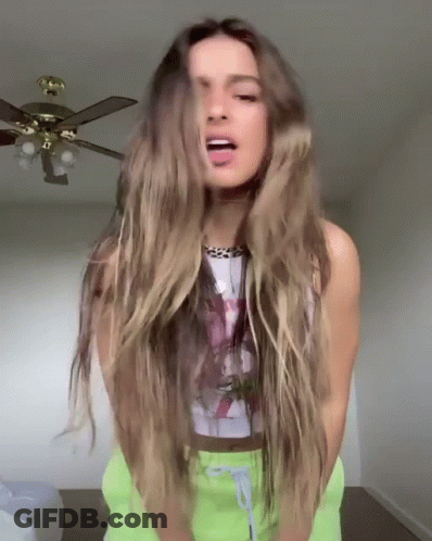 A Woman With Long Hair Is Standing In Front Of A Ceiling Fan And Sticking Out Her Tongue . GIF