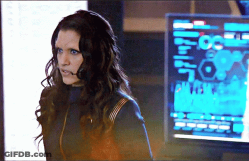 A Woman With Long Hair Is Standing In Front Of A Monitor That Says ' A ' On It . GIF