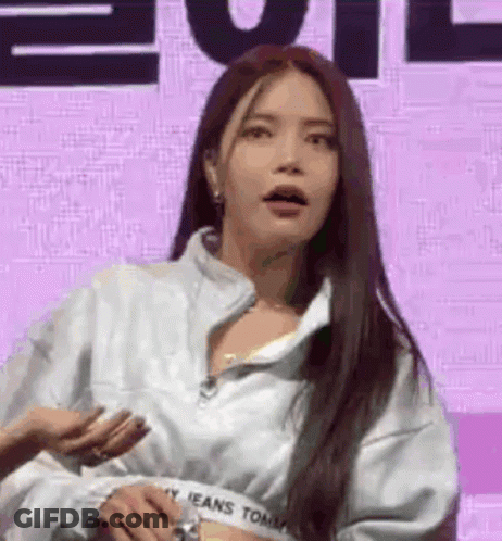 A Woman With Long Hair Is Standing In Front Of A Purple Background Wearing A White Jacket . GIF