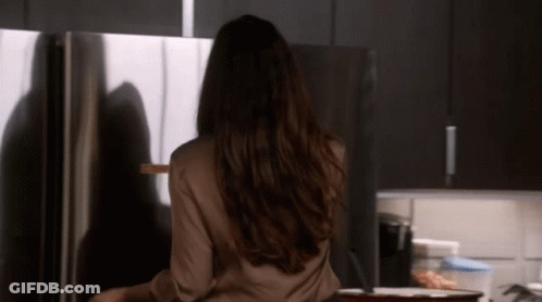 A Woman With Long Hair Is Standing In Front Of A Stainless Steel Refrigerator GIF