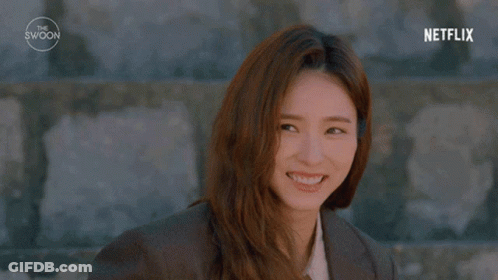 A Woman With Long Hair Is Standing In Front Of A Stone Wall . GIF