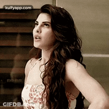 A Woman With Long Hair Is Standing In Front Of A Wall And Looking Up . GIF