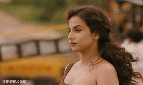 A Woman With Long Hair Is Standing In Front Of A Yellow School Bus . GIF