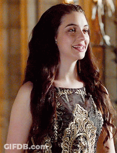 A Woman With Long Hair Is Wearing A Black And Gold Dress And Smiling GIF