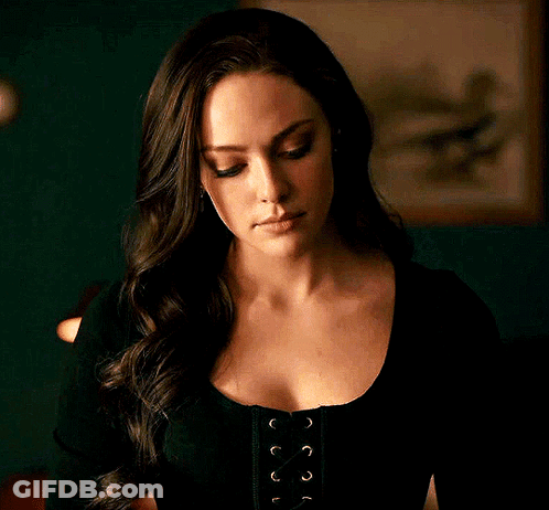A Woman With Long Hair Is Wearing A Black Lace Up Top And Looking At The Camera . GIF