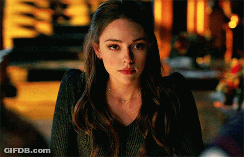 A Woman With Long Hair Is Wearing A Black Sweater And A Necklace . GIF