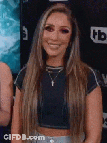A Woman With Long Hair Is Wearing A Crop Top And Smiling . GIF