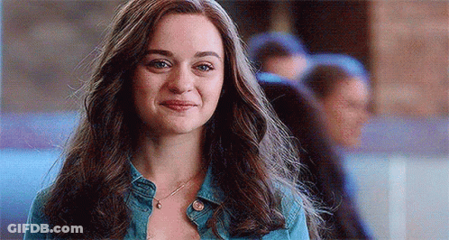 A Woman With Long Hair Is Wearing A Denim Jacket And A Necklace And Smiling . GIF