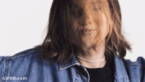 A Woman With Long Hair Is Wearing A Denim Jacket And A Necklace GIF