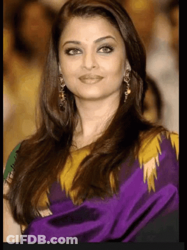 A Woman With Long Hair Is Wearing A Purple And Yellow Dress And Earrings . GIF