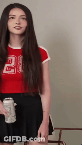 A Woman With Long Hair Is Wearing A Red Crop Top With The Number 28 On It GIF