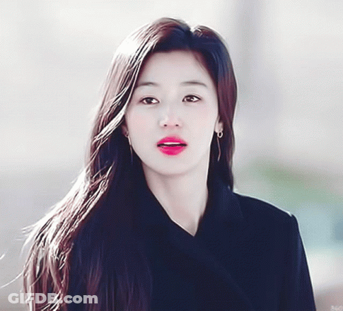 A Woman With Long Hair Is Wearing Earrings And A Black Coat GIF