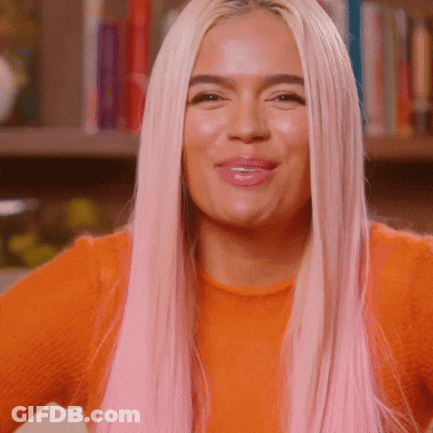 A Woman With Long Pink Hair Is Wearing An Orange Sweater And Smiling . GIF