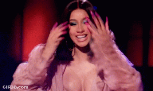 A Woman With Long Pink Nails And A Plunging Neckline Is Smiling While Holding Her Hair . GIF