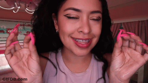 A Woman With Long Pink Nails And Braces On Her Teeth Smiles GIF