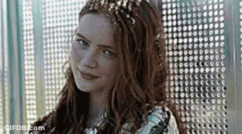 A Woman With Long Red Hair And A Crown On Her Head Is Standing In Front Of A Wall . GIF