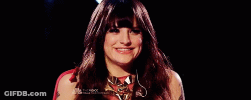 A Woman With Long Red Hair And Bangs Is Smiling In Front Of A Black Background . GIF