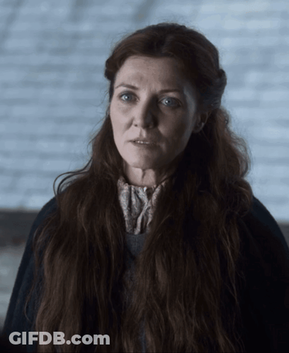 A Woman With Long Red Hair And Blue Eyes Is Wearing A Black Coat GIF