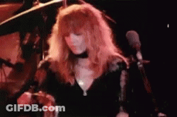 A Woman With Long Red Hair Is Singing Into A Microphone On Stage . GIF