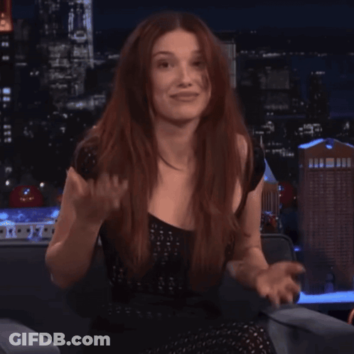 A Woman With Long Red Hair Is Sitting In Front Of A City Skyline GIF