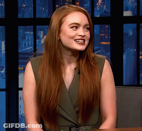 A Woman With Long Red Hair Is Smiling And Wearing A Green Dress GIF