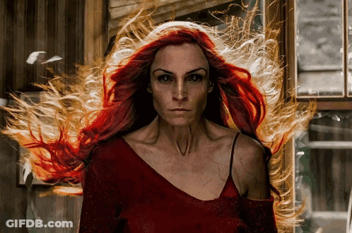 A Woman With Long Red Hair Is Standing In Front Of A Window With Fire Coming Out Of Her Hair GIF