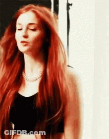 A Woman With Long Red Hair Is Wearing A Black Crop Top . GIF