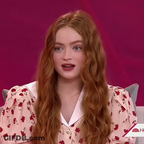 A Woman With Long Red Hair Is Wearing A Pink Floral Shirt GIF