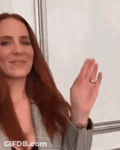 A Woman With Long Red Hair Is Wearing A Ring On Her Finger And Waving Her Hand . GIF