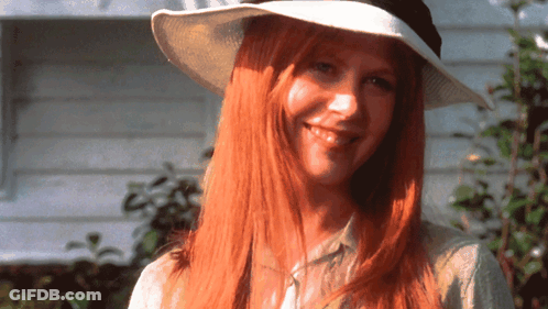 A Woman With Long Red Hair Is Wearing A White Hat And Smiling GIF