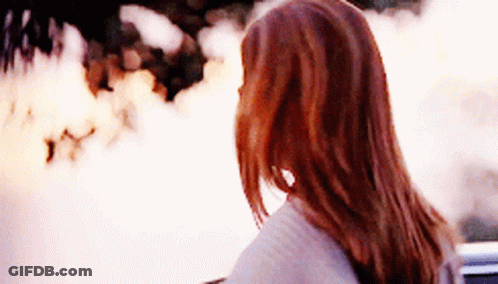 A Woman With Long Red Hair Looks At A Fire GIF