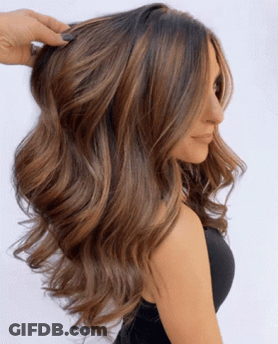 A Woman With Long Wavy Brown Hair Is Wearing A Black Top GIF